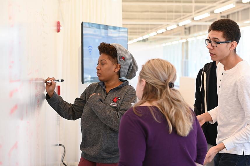 Three students working together on a white board inside the Idea Shop