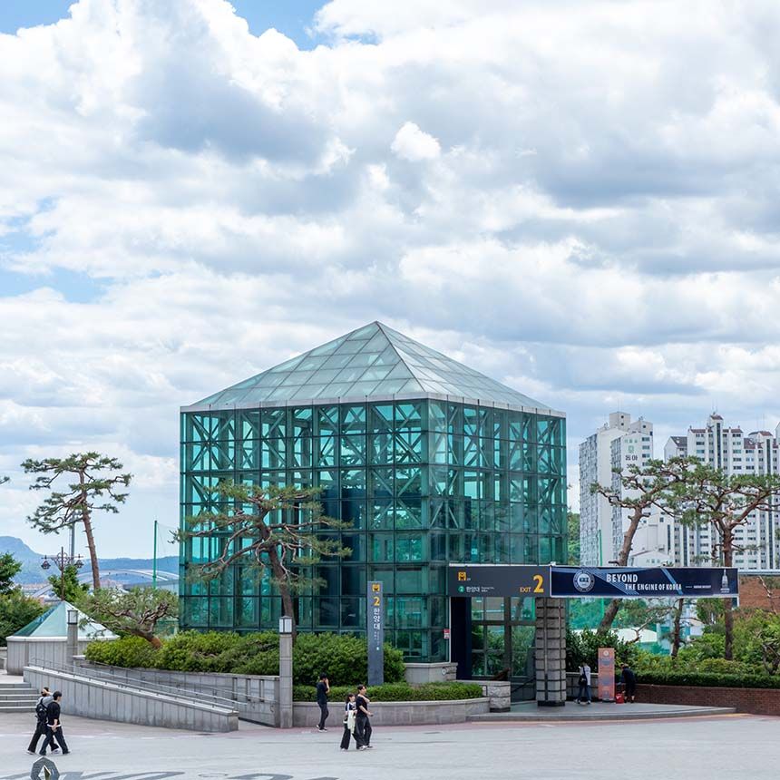 A modern glass and steel subway entrance at Hanyang University station with city buildings in the background.