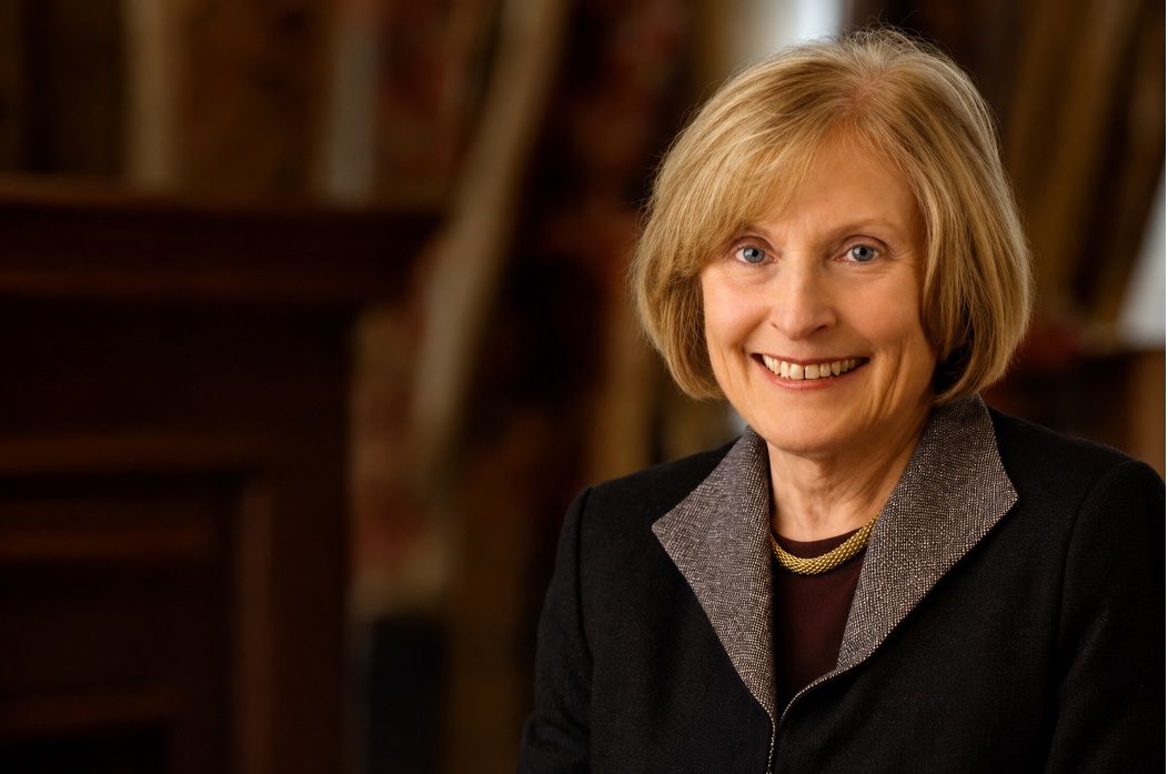 A woman wearing a dark jacket smiles for a portrait in front of a neutral background.